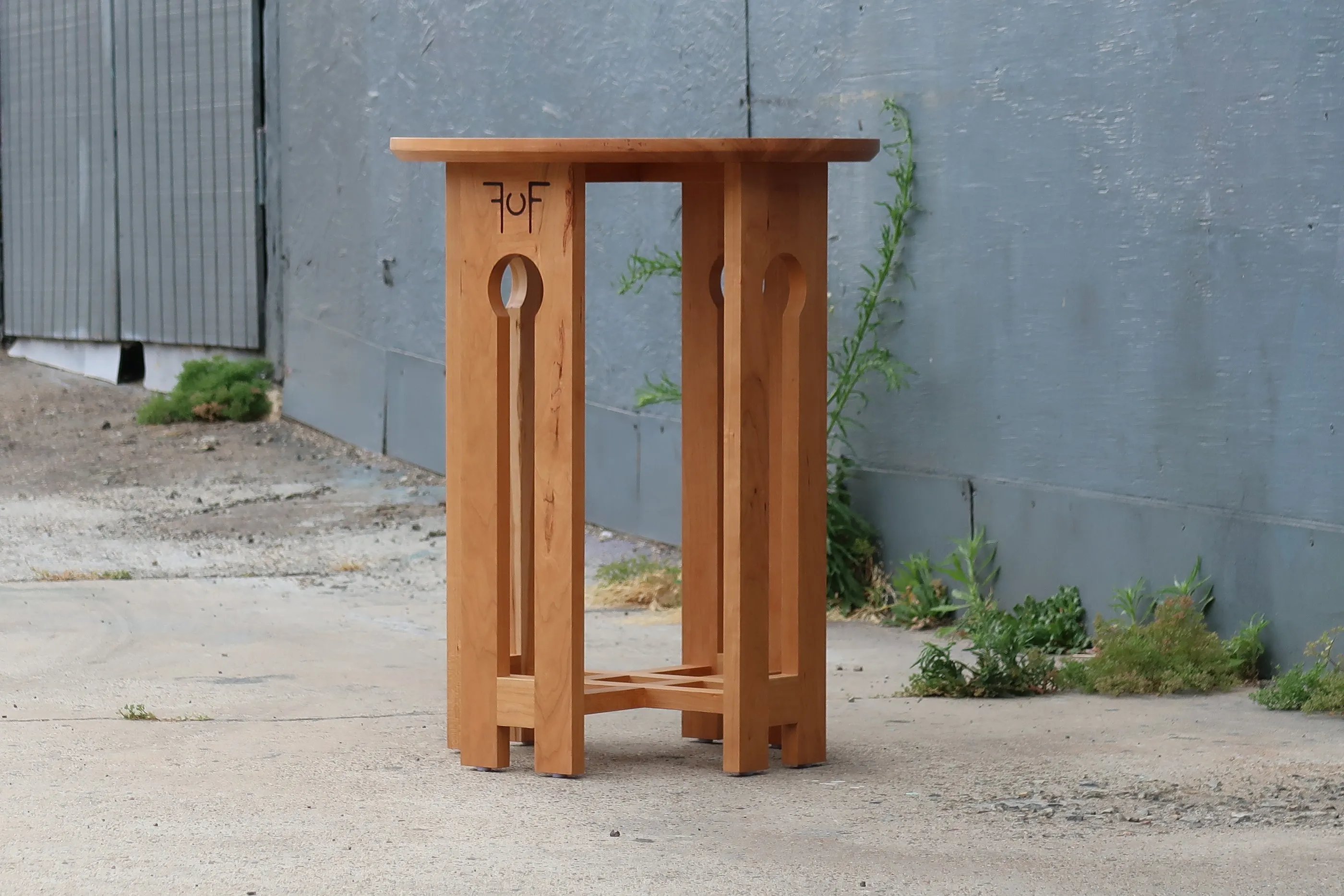 The craftsman end table at three-quarter view on a concrete slab, with the maker's mark branded into the frame below the top.