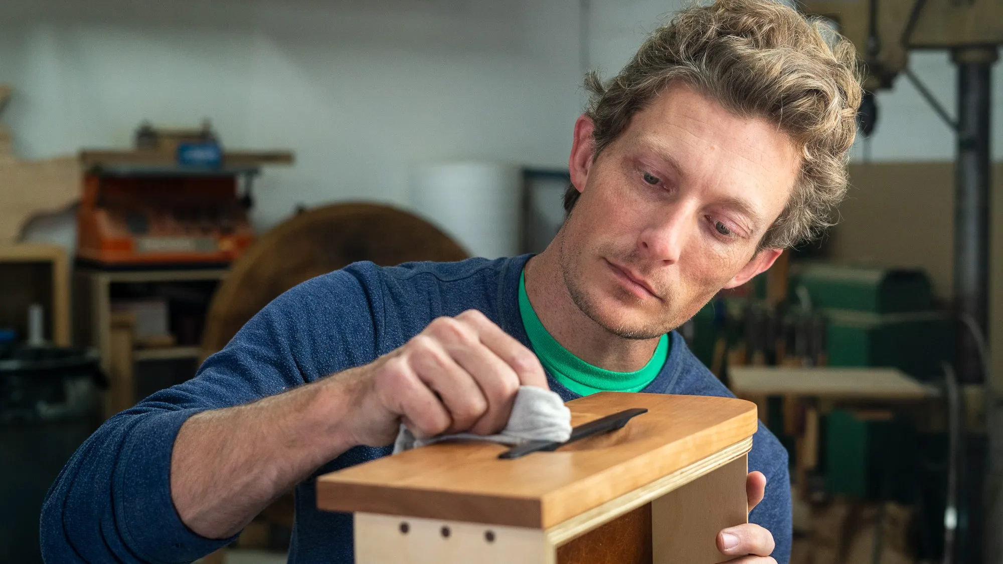 Bryan Ferris applying finish to a small cherry cabinet at his workbench in San Diego.
