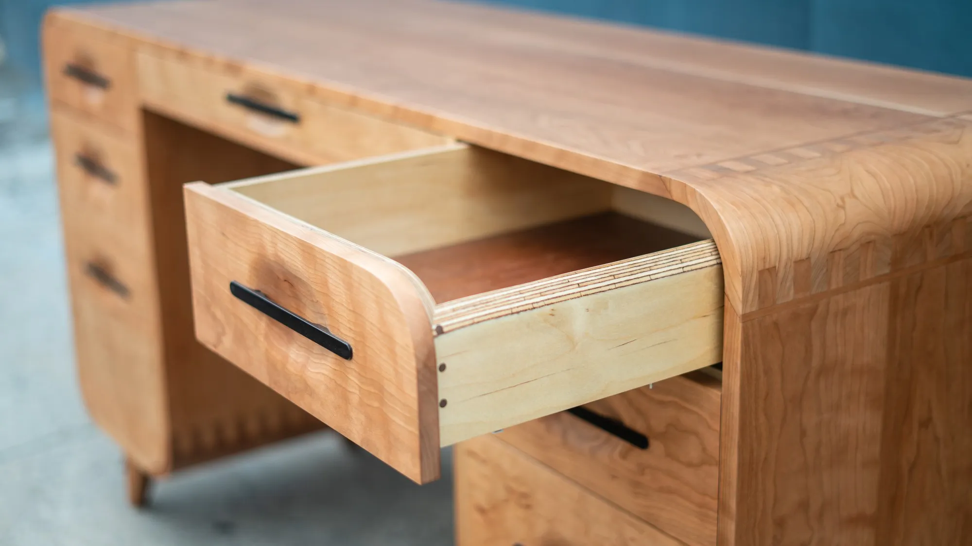 An open drawer of a solid cherry executive desk, showing the leather-lined bottom and an ebony pull set into a carved recess in the drawer front.