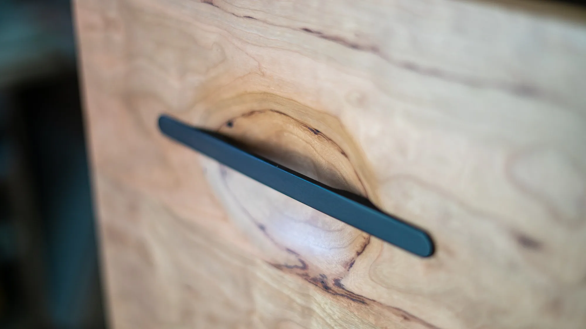 Close view of an ebony drawer pull set into a shallow hollow carved out of the cherry drawer front.