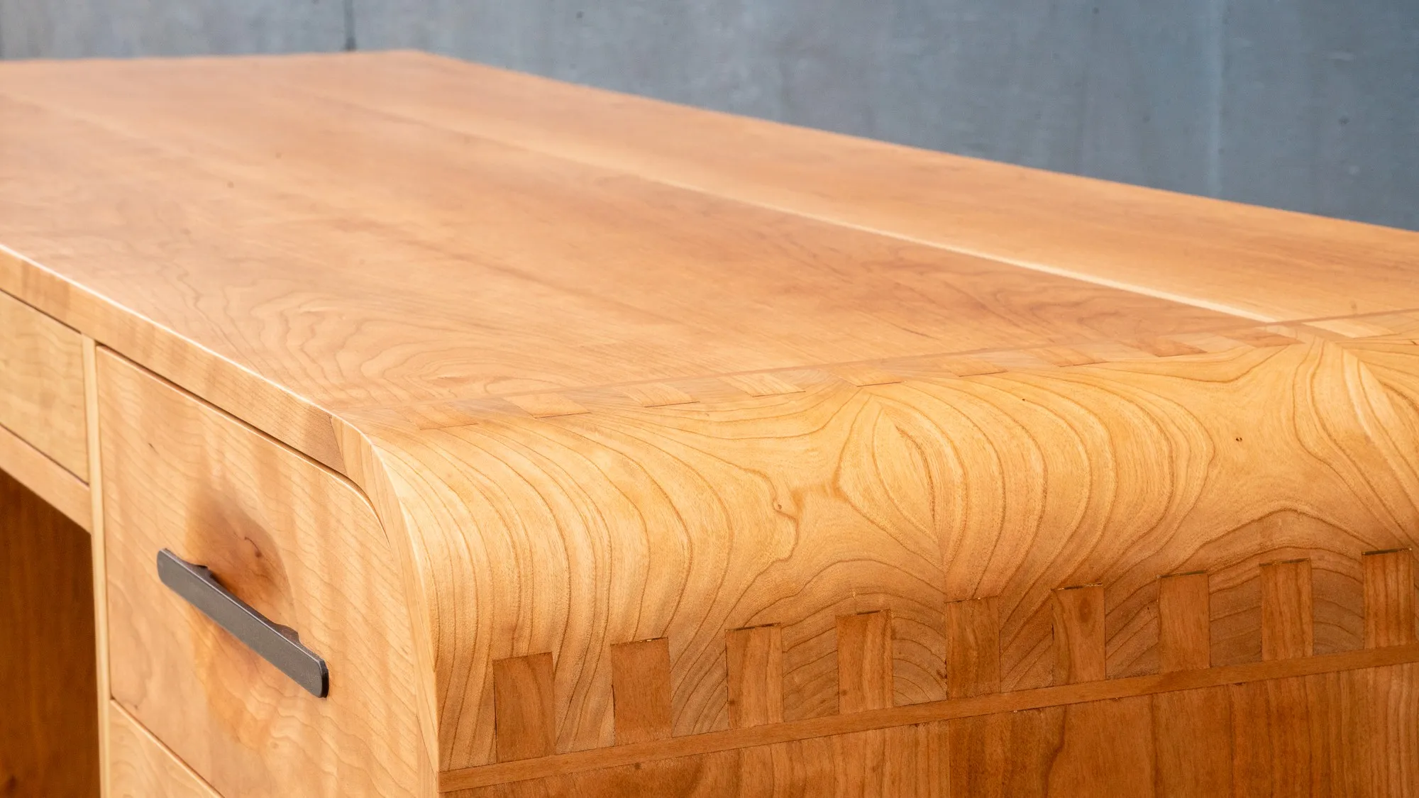The top of the cherry desk seen along its length, with figured grain running the full run and the finger joints visible along the front edge.